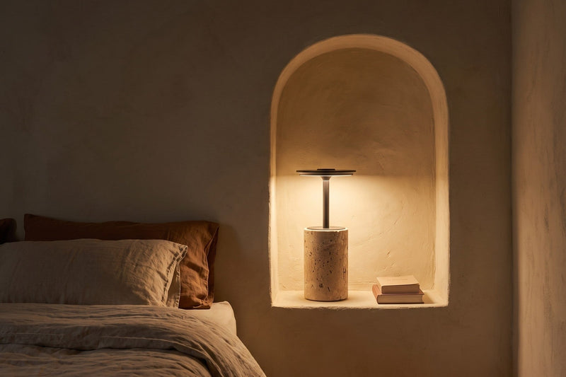 Lámpara sin cable Petra de travertino encendida en una hornacina de cal junto a la cama